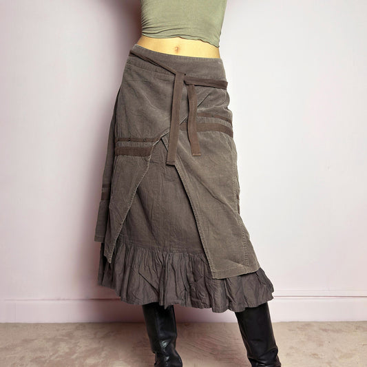 This vintage 2000s brown asymmetric midi skirt features a layered wrap design with a ruffle hem. Made from corduroy-cotton fabric, it includes tie closures for an adjustable fit, a back zipper closure, and subtle stitched detailing that adds a deconstructed touch. Perfect for earthy, bohemian, or avant-garde styling. It can be worn low rise for size M or high waisted for size L. Great vintage condition.