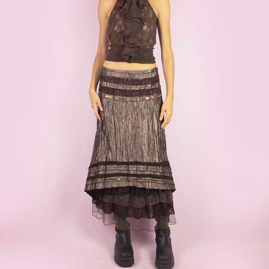 The Y2K Brown Layered Midi Skirt is a vintage 2000s piece featuring an earthy brown palette with a mix of crinkled fabric, lace, and mesh layers. The mid-waisted design and asymmetrical hemline create a flowy, bohemian silhouette, with a side zipper closure. Perfect for casual outings or whimsical evening looks.