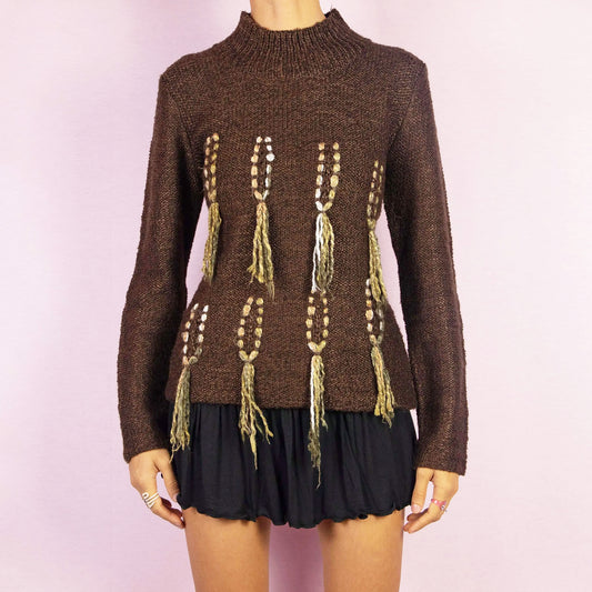 The Y2K Brown Turtleneck Sweater is a unique vintage 2000s warm pullover crafted from a cozy wool and acrylic blend. It features a turtleneck and standout embellishments with tassel details running vertically along the front. Perfect for any fall or winter wardrobe. Excellent vintage condition.