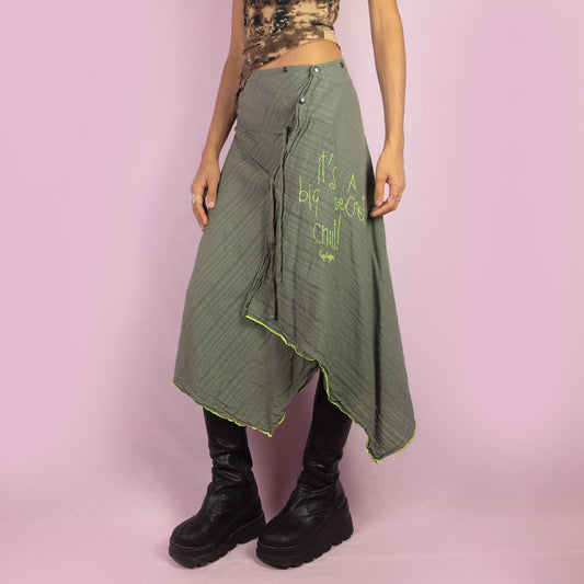 The Y2K Khaki Asymmetric Cop Copine Skirt is a unique vintage 2000s midi skirt showcasing the brand's signature avant-garde style. This high-waisted skirt features an asymmetrical hem and snap button detailing. Made with a lightweight fabric, it's an ideal choice for summer.