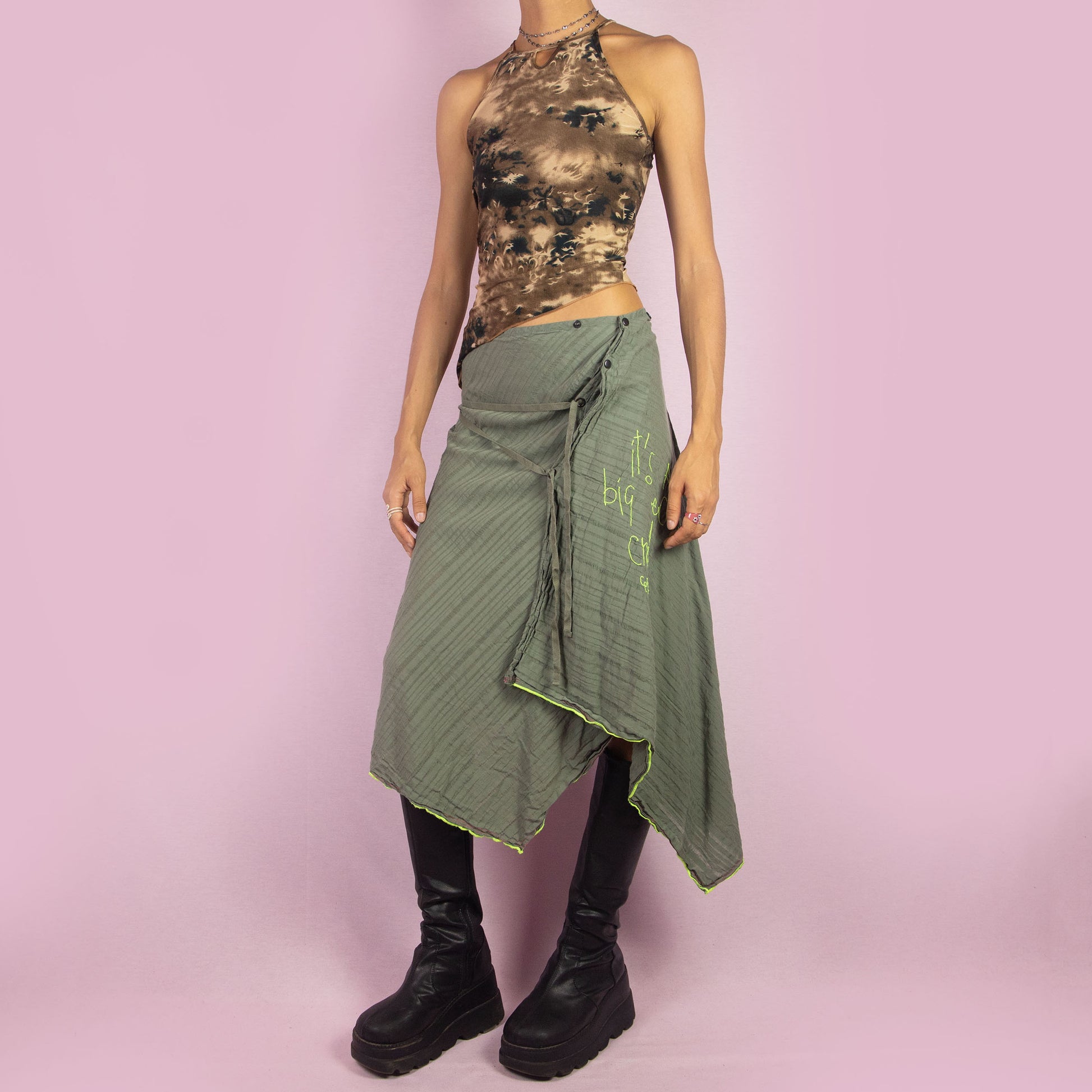 The Y2K Khaki Asymmetric Cop Copine Skirt is a unique vintage 2000s midi skirt showcasing the brand's signature avant-garde style. This high-waisted skirt features an asymmetrical hem and snap button detailing. Made with a lightweight fabric, it's an ideal choice for summer.