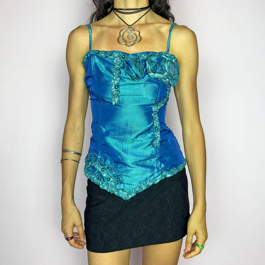 This vintage 2000s iridescent turquoise corset top features adjustable spaghetti straps, floral rosette appliqué, and beaded trim. The structured front sculpts the waist, while the ruched smocked back adds stretch and comfort. An asymmetrical hem and glossy finish elevate it for prom, weddings, or dreamy nights out. A romantic Y2K formal top that blends fairytale opulence with a bold, sculptural silhouette. Excellent vintage condition.