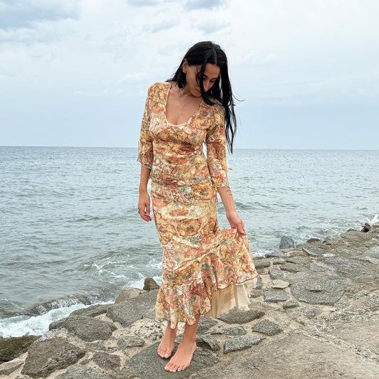 This vintage 2000s two-piece set features a cream-beige floral lace mesh with brown and blue accents. The asymmetric midi skirt has a flowing ruffle hem, paired with a matching semi sheer top with a scoop neckline and three-quarter tie bell sleeves. A whimsical spring-summer archival statement, ideal for parties, festivals, and seaside escapes. Made in Spain from polyester stretch mesh. Excellent vintage condition.