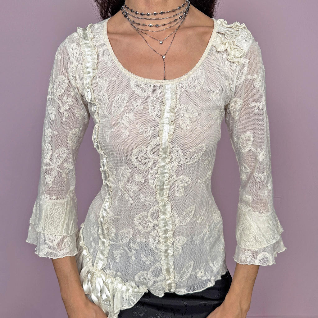 Soft romantic vintage 2000s cream white mesh blouse with floral embroidered details. 3/4 bell sleeves with ruffle cuffs, ruffle gathered seams, lace accents, and an asymmetric hem for an ethereal fairycore look. Statement blouse ideal for whimsical summer events. Stretchy fabric, 60% cotton and 40% polyester. Made in France by a French brand. Excellent vintage condition.