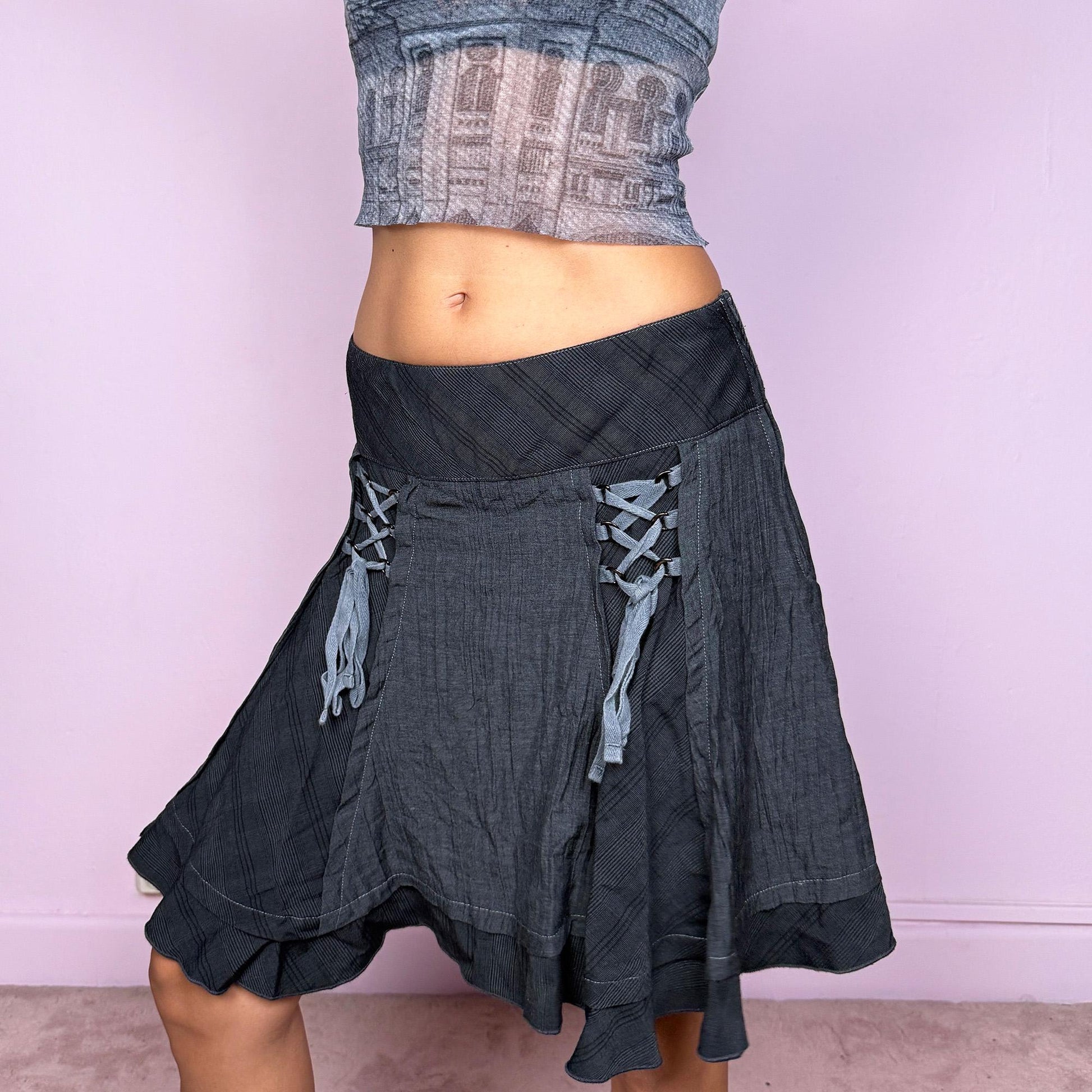 This vintage 2000s dark gray flared mini skirt features a ruffle hem, side zipper closure, and tie-front lace-up details. With subtle medievalcore inspiration, it blends whimsical fairy goth elegance with party allure, perfect for night events or romantic streetwear styling. Can be worn low-rise in S or mid-rise in M for adjustable fit. Great vintage condition.