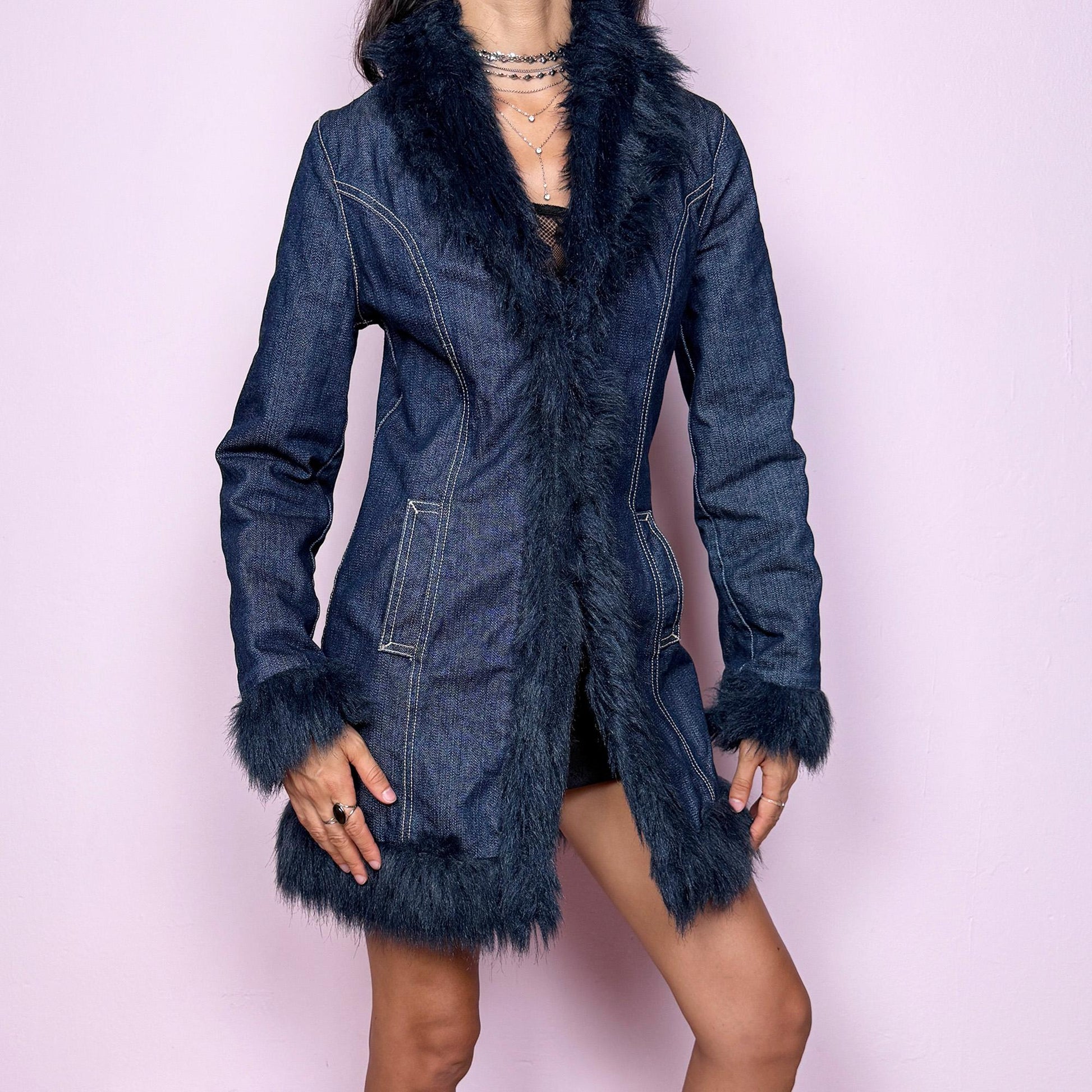 This vintage 2000s dark blue denim Penny Lane coat features deep navy faux fur trim along the collar, cuffs, and hem. Designed with front pockets and button closure, it blends 70s-inspired boho charm with Y2K streetwear edge. The fitted cut and rich indigo tone make it the ultimate statement winter coat—perfect for city styling or retro layering. Made from a cotton polyester denim blend with faux fur trim. Excellent vintage condition.