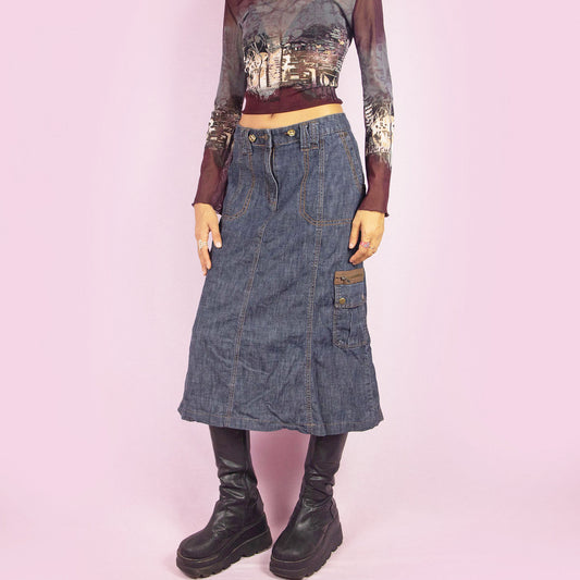 The Y2K Denim Cargo Midi Skirt is a vintage 2000s piece featuring a mid-rise silhouette, pockets, a side cargo pocket, and a front zipper closure. Perfect for casual outfits and everyday wear.