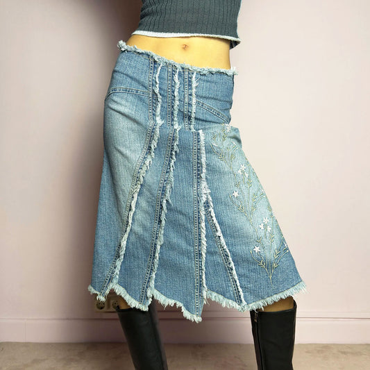 The Y2K Denim Patchwork Midi Skirt is a vintage 2000s statement piece featuring a deconstructed patchwork denim design with raw frayed edges, a panel construction that creates a flared silhouette and delicate floral embroidery. Finished with a high-waisted fit, asymmetrical hem, and a side zipper closure, this skirt is perfect for fairy grunge, bohemian, and eclectic outfits.