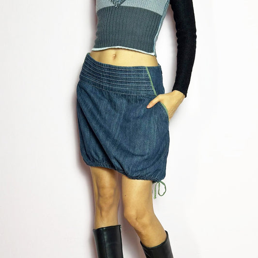 The Y2K Denim Bubble Mini Skirt is a vintage 2000s piece featuring a dark wash denim with unique structured pleating at the waist. Designed with an adjustable bubble hem with drawstrings for a customizable fit, this skirt blends playful and edgy aesthetics. It also includes a side zipper closure. Perfect for statement streetwear looks.
