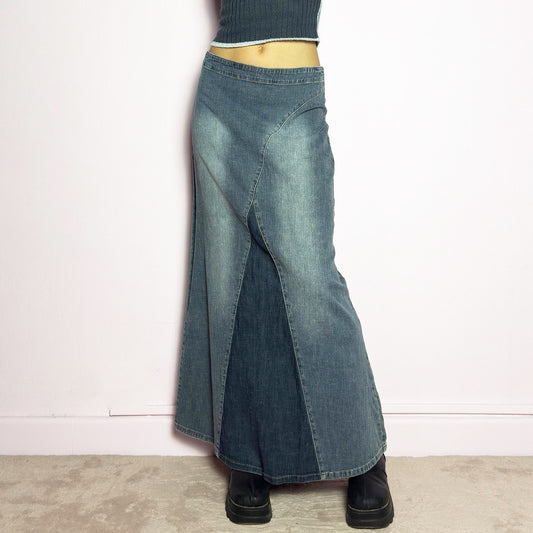 The Y2K Denim Paneled Maxi Skirt is a vintage 2000s piece featuring a unique paneled design with contrast wash details. Crafted from structured stretchy denim, this skirt offers a flattering mid-rise fit with a sleek, flared silhouette. Designed with a back zipper closure and a subtle back slit for ease of movement, it's perfect for casual streetwear outfits.