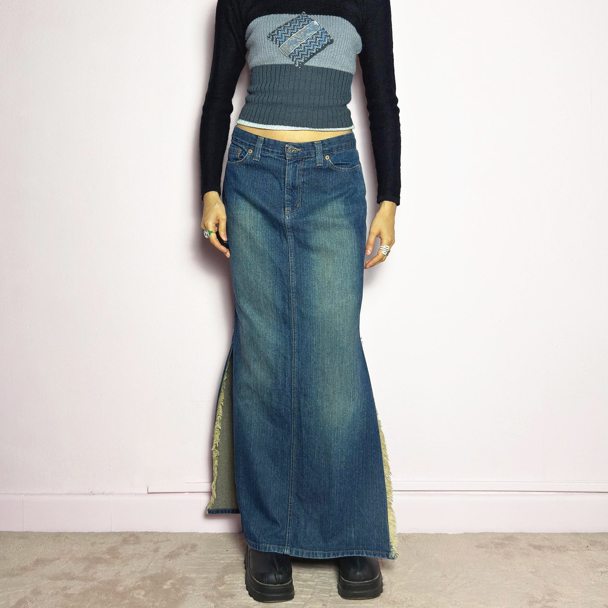 The Y2K Denim Side Slit Maxi Skirt is a vintage 2000s statement piece featuring a structured mid-rise fit and a sleek, elongated silhouette. Designed with frayed side slit details, a button and zipper closure, and classic five-pocket styling, this skirt is perfect for casual streetwear looks. Excellent vintage condition.