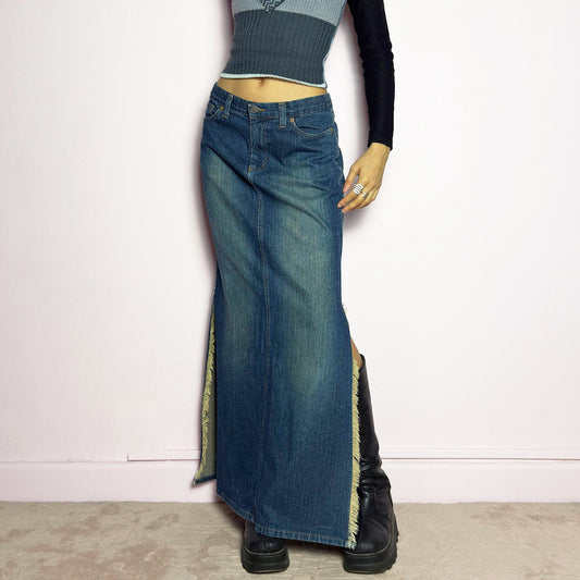 The Y2K Denim Side Slit Maxi Skirt is a vintage 2000s statement piece featuring a structured mid-rise fit and a sleek, elongated silhouette. Designed with frayed side slit details, a button and zipper closure, and classic five-pocket styling, this skirt is perfect for casual streetwear looks.