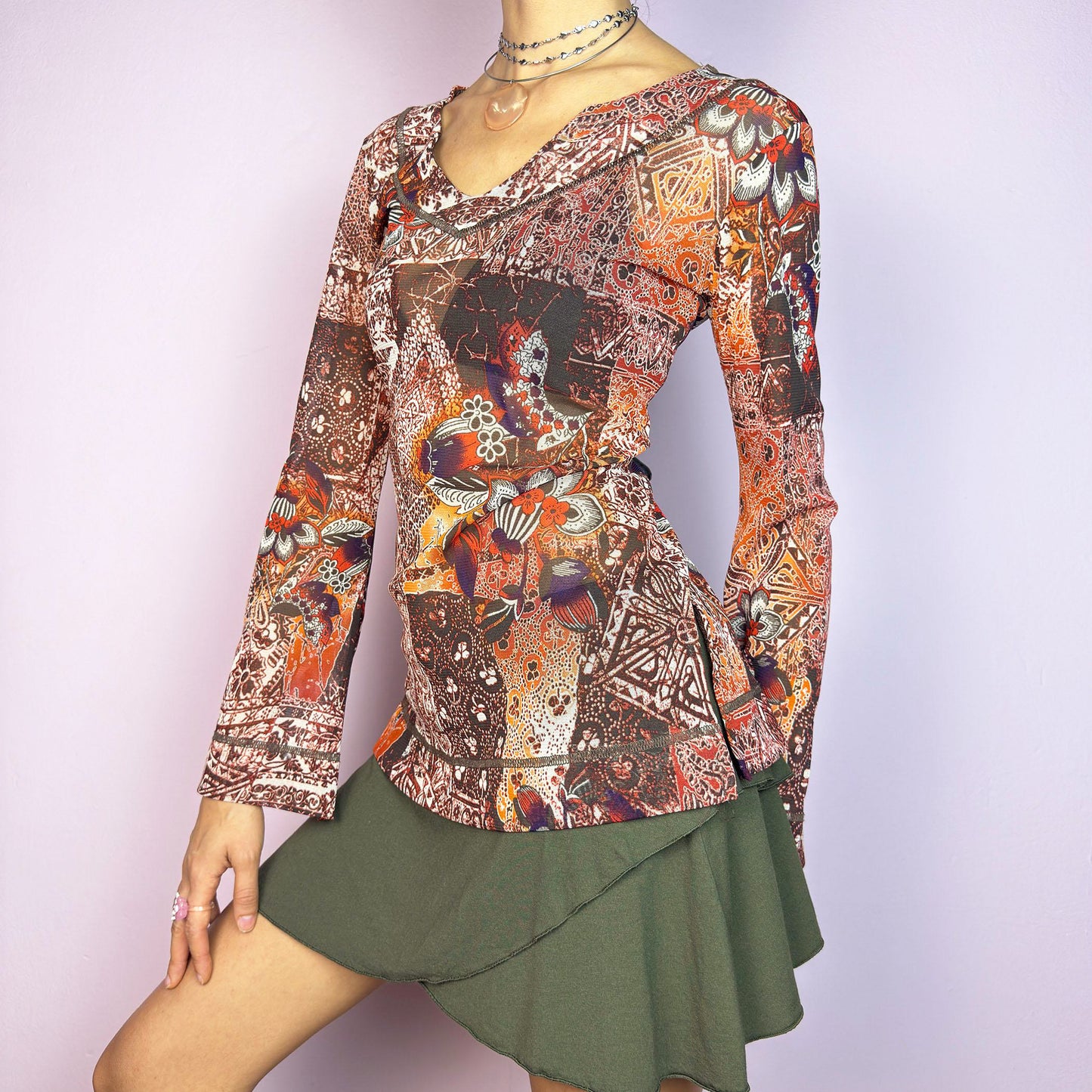 The Y2K Mesh Flared Long Sleeve Top is a vibrant vintage 2000s piece, featuring a floral and paisley print in earthy tones of orange, red, and brown. Crafted from lightweight mesh fabric, this top has a semi-sheer finish and flared long sleeves. Perfect for a whimsical, boho-inspired outfit. Excellent vintage condition.