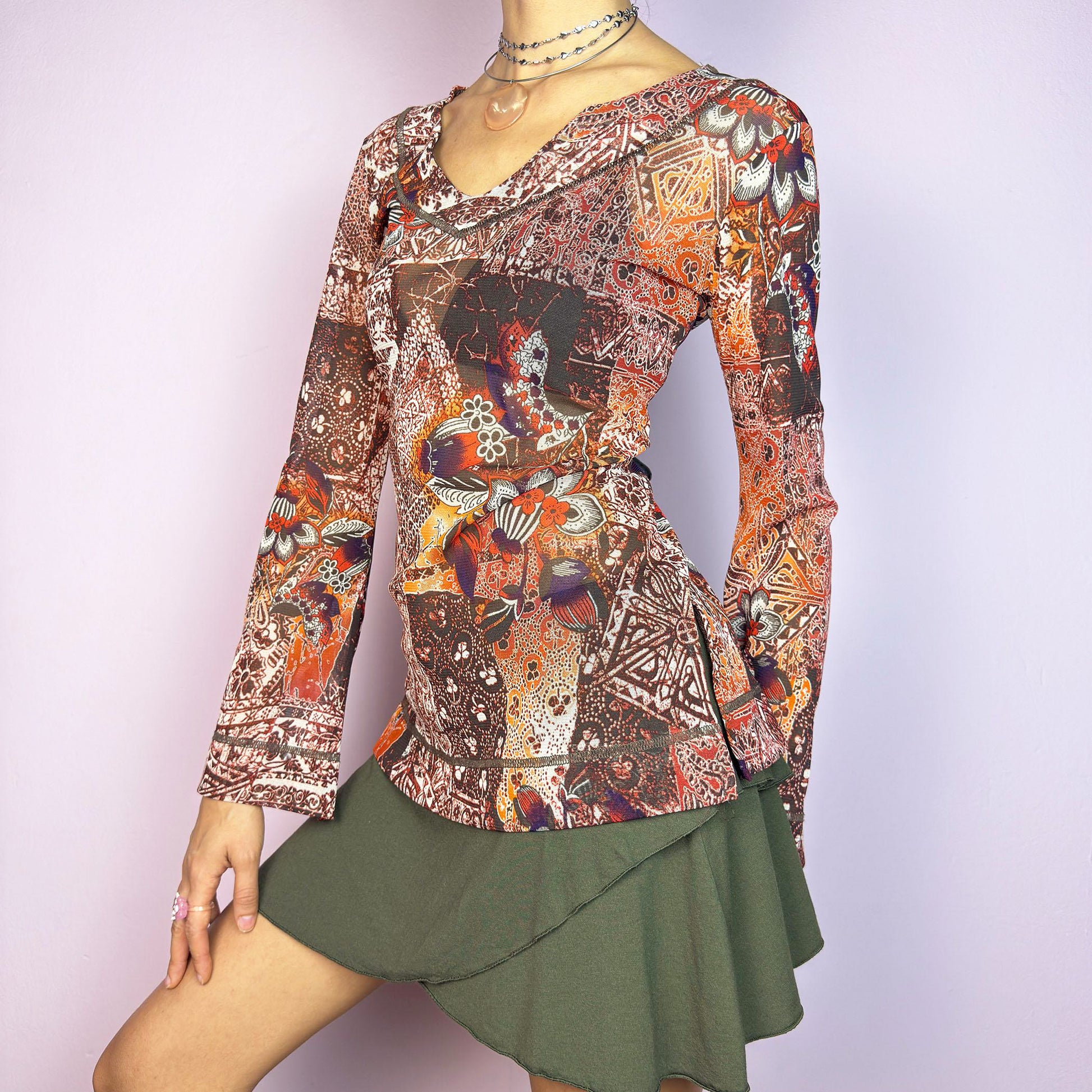 The Y2K Mesh Flared Long Sleeve Top is a vibrant vintage 2000s piece, featuring a floral and paisley print in earthy tones of orange, red, and brown. Crafted from lightweight mesh fabric, this top has a semi-sheer finish and flared long sleeves. Perfect for a whimsical, boho-inspired outfit. Excellent vintage condition.