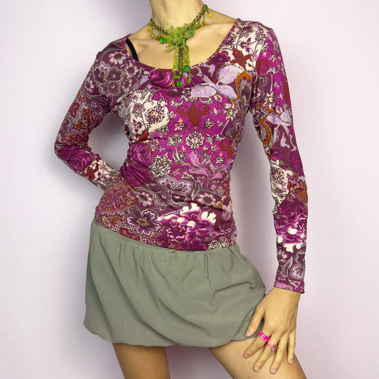 The Y2K Floral Paisley Print Top is a vintage 2000s long-sleeve piece featuring a vibrant mix of floral and paisley patterns in shades of purple, pink, and burgundy. Designed with a flattering body-hugging fit and a scoop neckline, this soft and stretchy top is perfect for casual boho-inspired outfits. Excellent vintage condition.