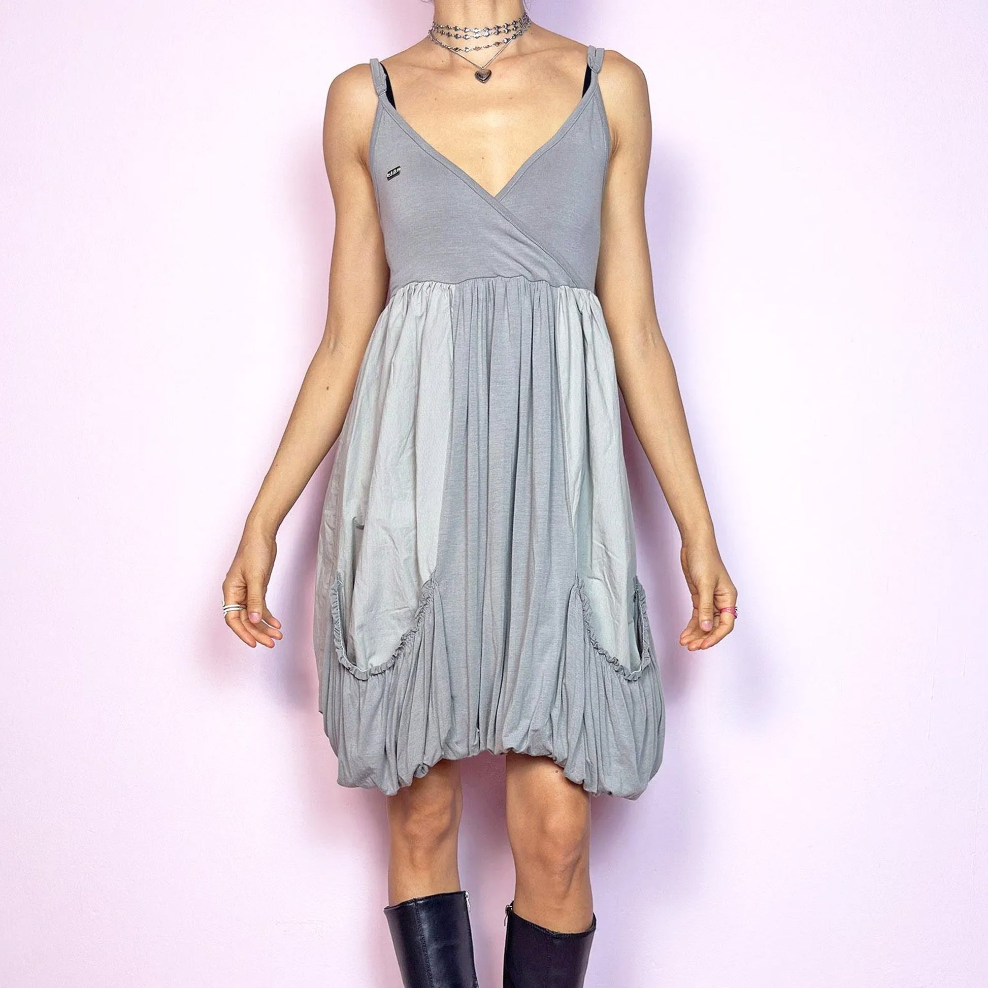 This vintage 2000s mini dress features a soft grey palette, deep wrap V-neckline, and empire waist with adjustable straps and light stretch. The voluminous bubble hem and oversized ruched pockets create sculptural movement and playful volume. Perfect for summer. A cyber-futuristic, deconstructed silhouette—airy, offbeat, and effortlessly cool. Excellent vintage condition.