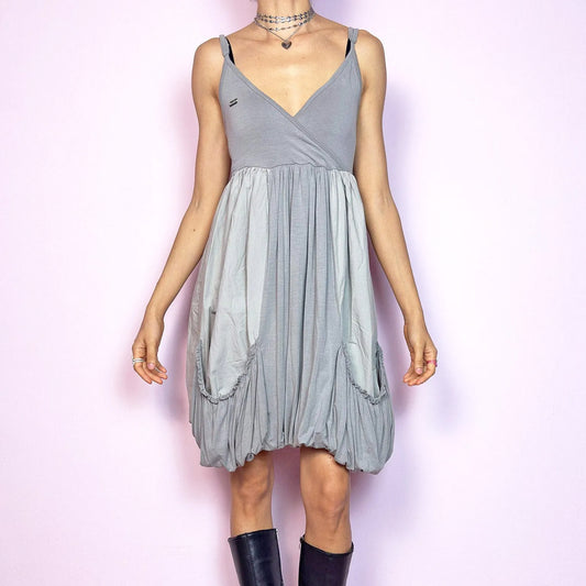 This vintage 2000s mini dress features a soft grey palette, deep wrap V-neckline, and empire waist with adjustable straps and light stretch. The voluminous bubble hem and oversized ruched pockets create sculptural movement and playful volume. Perfect for summer. A cyber-futuristic, deconstructed silhouette—airy, offbeat, and effortlessly cool. Excellent vintage condition.