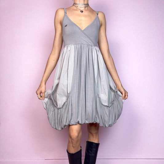 This vintage 2000s mini dress features a soft grey palette, deep wrap V-neckline, and empire waist with adjustable straps and light stretch. The voluminous bubble hem and oversized ruched pockets create sculptural movement and playful volume. Perfect for summer. A cyber-futuristic, deconstructed silhouette—airy, offbeat, and effortlessly cool. Excellent vintage condition.