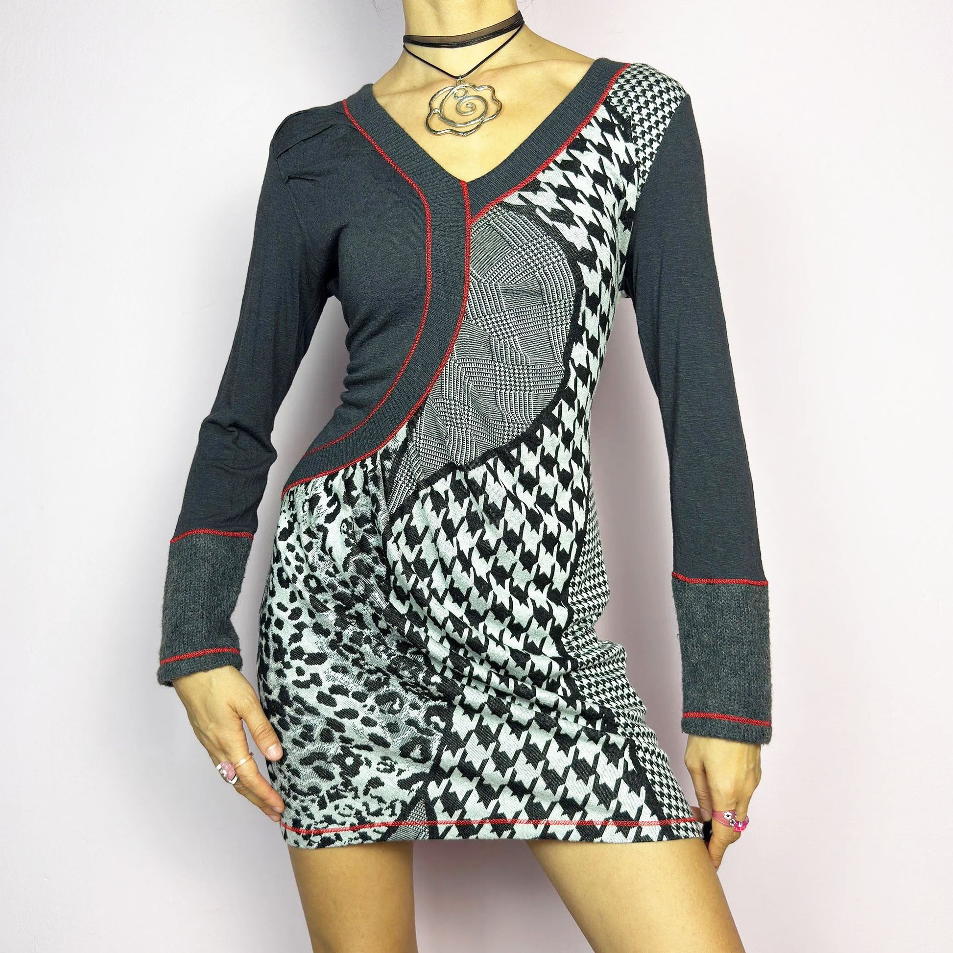 The Y2K Gray Patchwork Mini Dress is a vintage 2000s piece featuring a bold patchwork print with a mix of houndstooth, plaid, and leopard patterns, a V-neckline and long sleeves. The fitted silhouette is accentuated with contrast red stitching. Made from a stretchy fabric, it offers a flattering fit. Ideal for casual streetwear or a night-out ensemble.