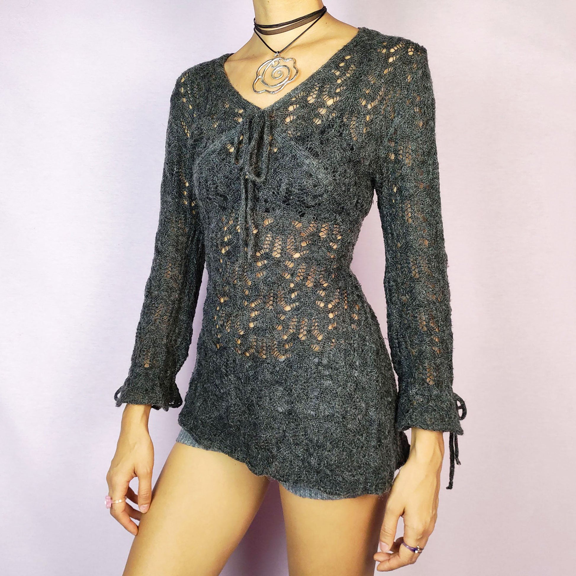 The Y2K Gray Sheer Sweater is a vintage 2000s pullover featuring a delicate knit pattern with semi-sheer details, offering a lightweight yet cozy feel. Designed with three quarter sleeves and a tie detail at the neckline, this sweater provides a flattering, fitted silhouette. Perfect for casual or dressier outfits.
