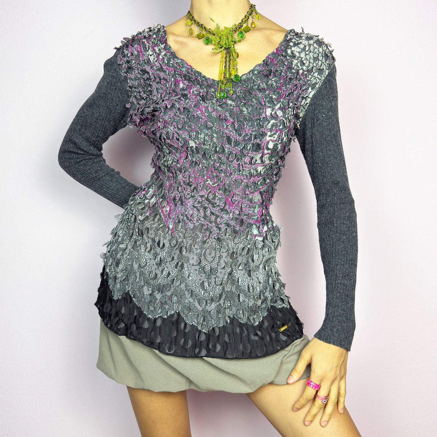 The Y2K Gray Crinkled Textured Top is a vintage 2000s piece by designer Roberto Verino, featuring a unique sheer overlay with delicate cut-out details that create a dimensional, deconstructed look. The long knit sleeves contrast beautifully with the intricate textures, adding depth to this stretchy fit design. A standout piece for those who love avant-garde fashion.