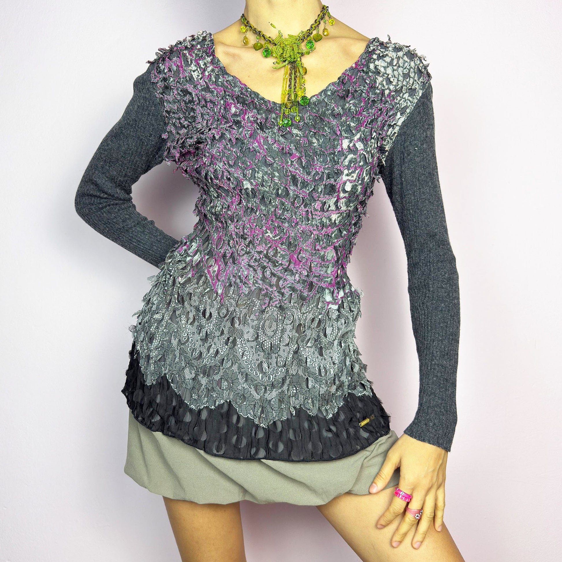 The Y2K Gray Crinkled Textured Top is a vintage 2000s piece by designer Roberto Verino, featuring a unique sheer overlay with delicate cut-out details that create a dimensional, deconstructed look. The long knit sleeves contrast beautifully with the intricate textures, adding depth to this stretchy fit design. A standout piece for those who love avant-garde fashion.