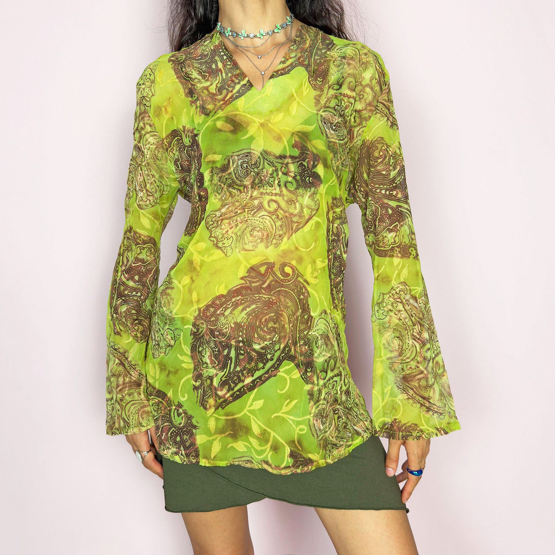 This vintage 2000s bohemian sheer green blouse casts a psychedelic glow with swirling brown paisley motifs and fluid draping. Flared long sleeves and a soft V-neckline evoke carefree elegance. Wear it layered at summer parties or as a lightweight, kaftan-inspired beach cover-up. Made in France from lightweight polyester. Excellent vintage condition.