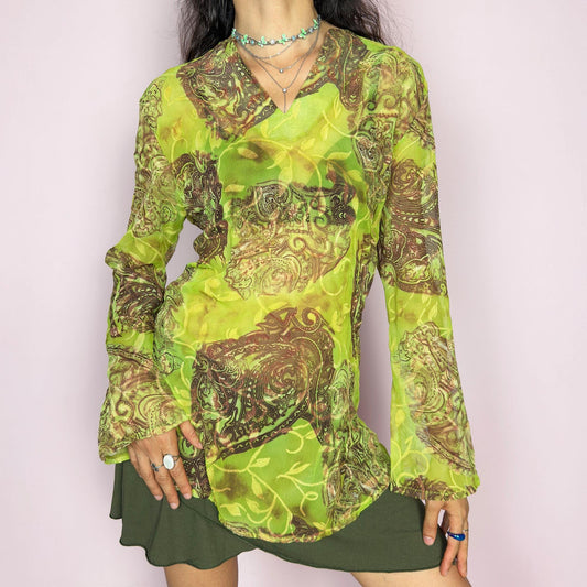 This vintage 2000s bohemian sheer green blouse casts a psychedelic glow with swirling brown paisley motifs and fluid draping. Flared long sleeves and a soft V-neckline evoke carefree elegance. Wear it layered at summer parties or as a lightweight, kaftan-inspired beach cover-up. Made in France from lightweight polyester. Excellent vintage condition.