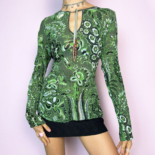 The Y2K Green Boho Tie Front Top is a vintage 2000s piece featuring an abstract floral print on lightweight, semi-sheer fabric. Designed with a front keyhole neckline and adjustable tie adorned with wooden bead details. The long sleeves and breathable material make it comfy and flattering. A unique top perfect for summer layering, festival outfits, fairy grunge, or earthy boho styles.