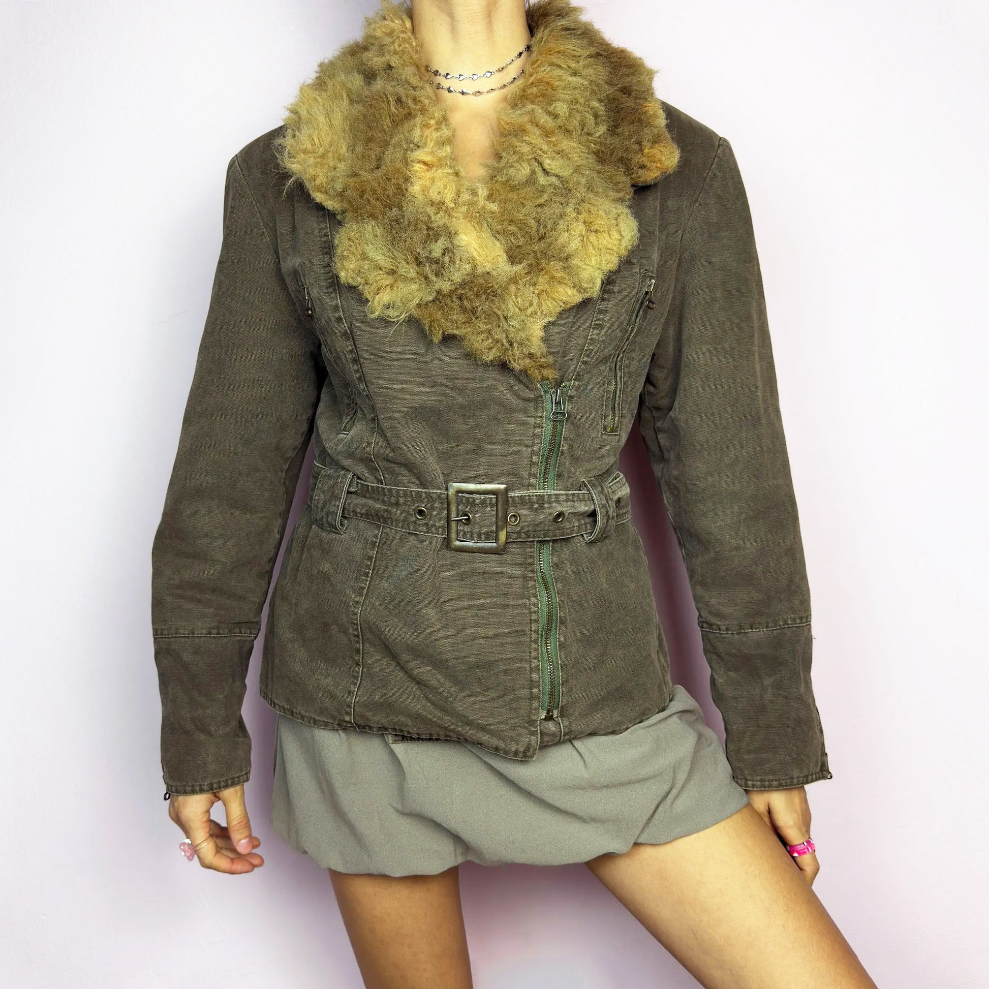 The Y2K Khaki Belted Jacket is a vintage 2000s piece featuring a structured fit with rugged utility-inspired details. Designed with padded shoulders for a strong silhouette, an oversized plush faux-shearling collar, asymmetric zip closure, and an adjustable waist belt for a cinched look. The washed khaki tone and distressed finish add to its edgy, worn-in appeal, making it perfect for grunge or military-inspired winter outfits. A bold outerwear piece for layering in colder seasons. Great vintage condition.