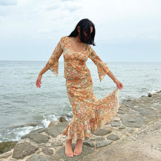 This vintage 2000s two-piece set features a cream-beige floral lace mesh with brown and blue accents. The asymmetric midi skirt has a flowing ruffle hem, paired with a matching semi sheer top with a scoop neckline and three-quarter tie bell sleeves. A whimsical spring-summer archival statement, ideal for parties, festivals, and seaside escapes. Made in Spain from polyester stretch mesh. Excellent vintage condition.