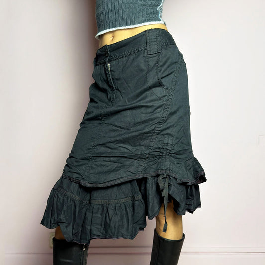 The Y2K Black Layered Skirt by Marithé François Girbaud is a vintage 2000s statement piece featuring a structured design with ruched details and ruffled layers for added texture and movement. Designed with a mid-rise fit, button and zipper closure, embroidered side detail, and an asymmetrical hem, this skirt blends edgy streetwear vibes with a playful, gothic aesthetic. Perfect for casual grunge and alternative looks. Excellent vintage condition.