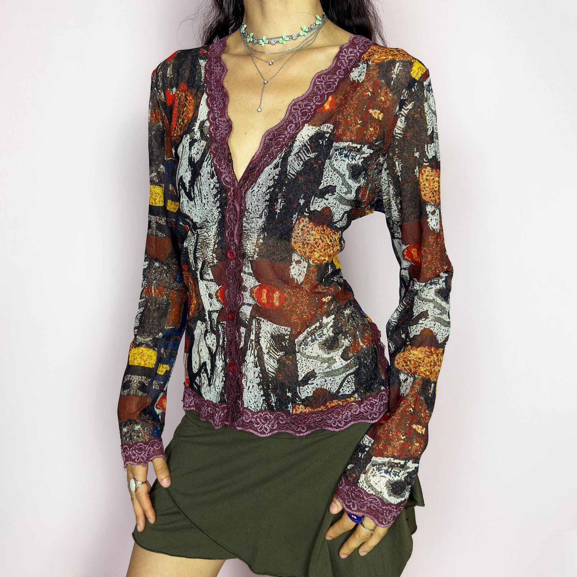 The vintage 2000s mesh sheer blouse features an abstract painting print in burnt orange, ochre, red, and charcoal. Made of stretch polyester mesh, it has long sleeves, a deep V-neckline trimmed in plum lace, and a tonal button front. This top is a rare avant garde piece with a romantic, artsy edge—perfect for chic events, layering, and transitional weather. Excellent vintage condition.