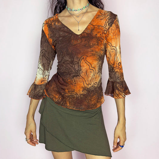 This vintage 2000s mesh top features semi-sheer three-quarter bell sleeves and a deep V-neckline. The fitted silhouette is printed with a burnt orange and brown tie-dye paisley motif, accented by fine gold glitter for subtle shimmer. Made in France, it’s a dreamy piece for romantic, boho, or fairy grunge wardrobes. Made from stretch polyester blend. Excellent vintage condition.