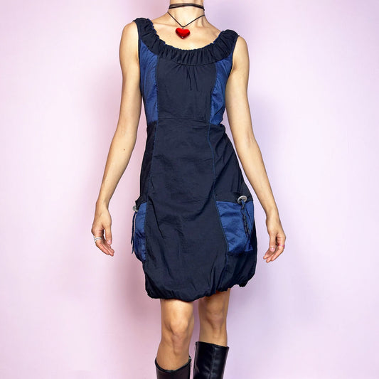 The Y2K Navy &amp; Black Bubble Mini Dress is a bold vintage 2000s statement piece with utility-inspired vibes. Features a unique bubble hem, ruched scoop neckline, and structured paneled design with contrast navy inserts. Equipped with chunky side pockets and metal ring details for an industrial touch. Made from a stretchy fabric with a techy texture. Perfect for dystopian streetwear, cyber grunge, or Harajuku styling. Great vintage condition.