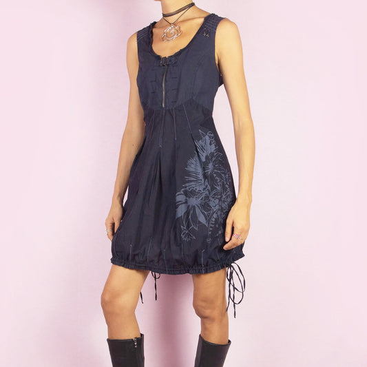 The Y2K Blue Bubble Mini Dress is a vintage 2000s piece featuring a lightweight cotton fabric with a floral print accent on the skirt and a structured, sleeveless bodice with a front zipper and buckle detail. The bubble hemline, with adjustable drawstring ties, adds a unique and playful silhouette. Perfect for summer outings or evening looks.