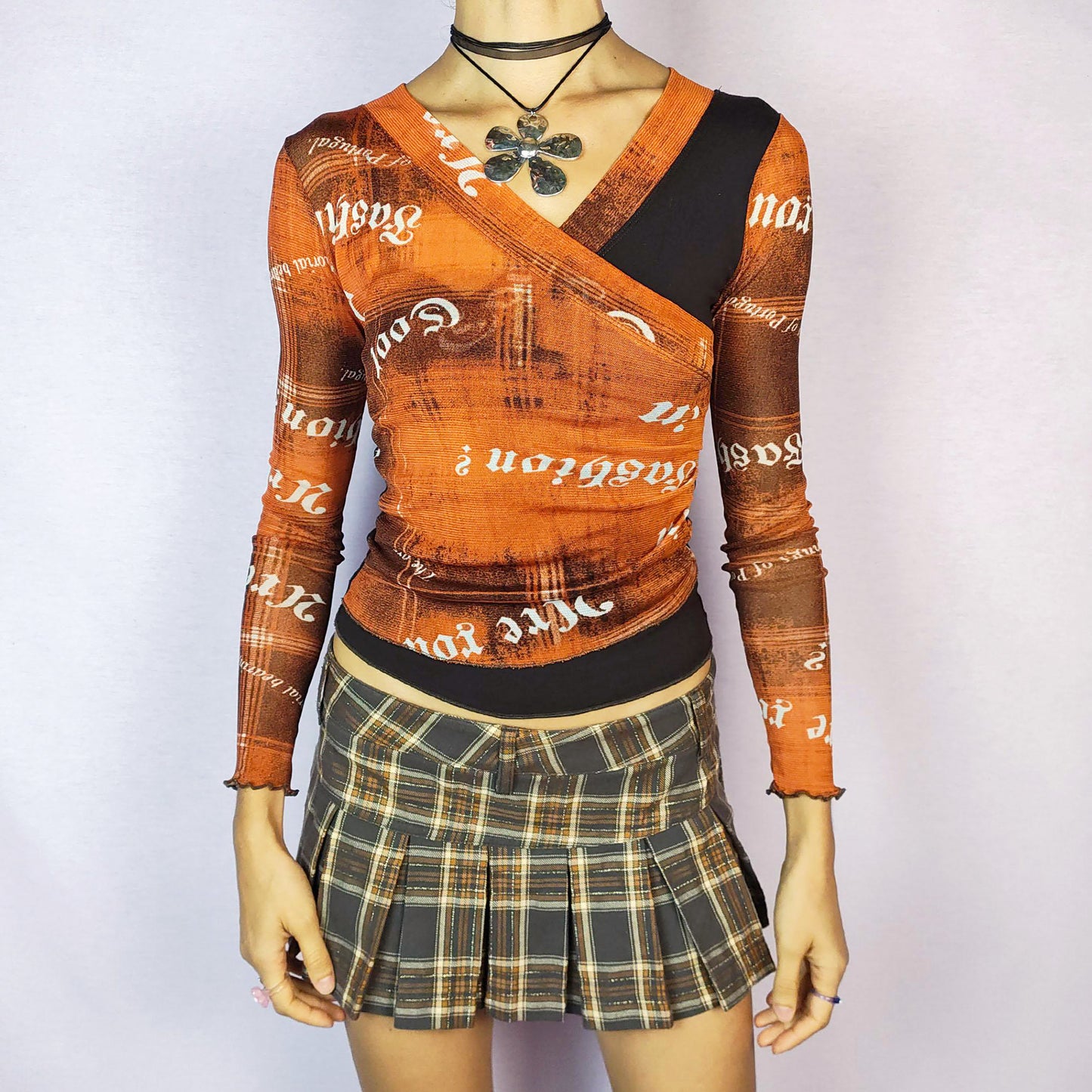 The Y2K Print Mesh Wrap Top is a vintage 2000s piece featuring a vibrant orange and brown design with bold typography prints. Crafted from a lightweight mesh fabric, it has a wrap-style front that accentuates the silhouette and long sleeves with lettuce hems for added detail. Perfect for casual outfits. Great vintage condition.