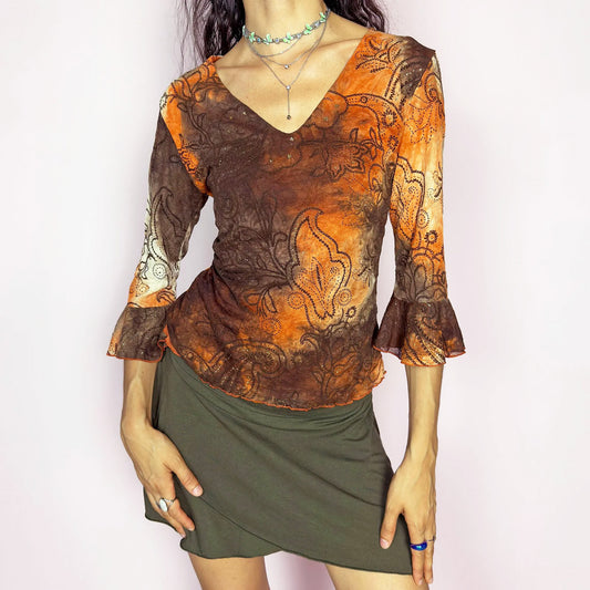 This vintage 2000s mesh top features semi-sheer three-quarter bell sleeves and a deep V-neckline. The fitted silhouette is printed with a burnt orange and brown tie-dye paisley motif, accented by fine gold glitter for subtle shimmer. Made in France, it’s a dreamy piece for romantic, boho, or fairy grunge wardrobes. Made from stretch polyester blend. Excellent vintage condition.