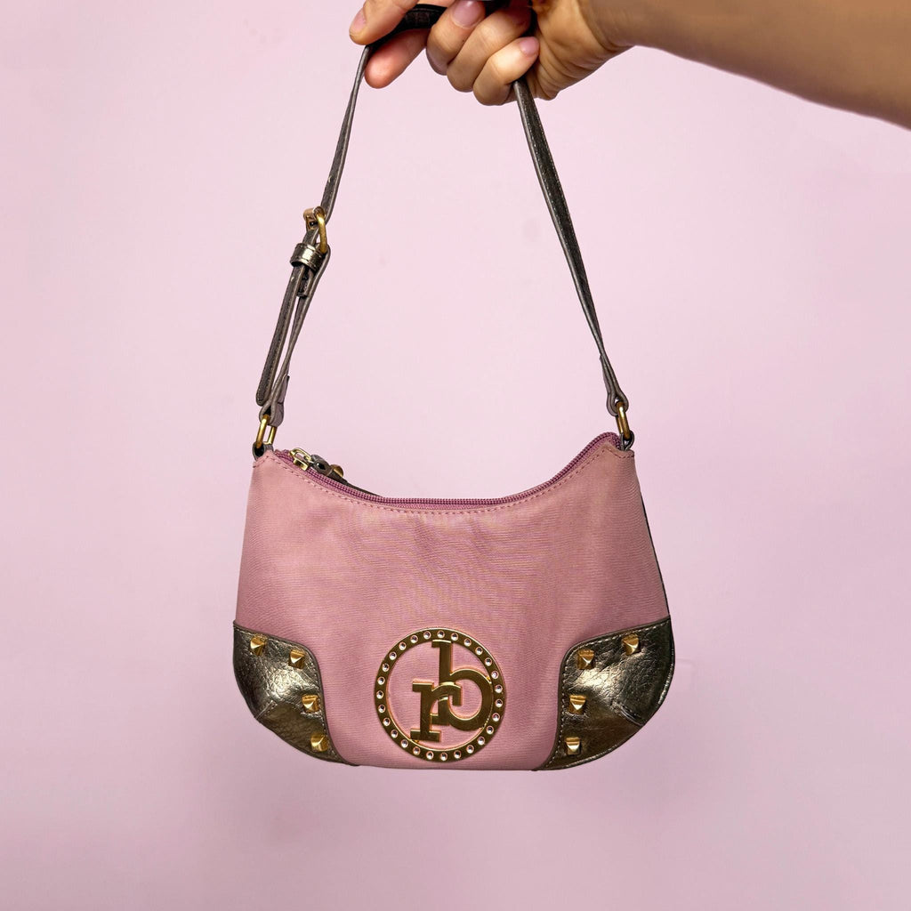 Vintage Y2K dusty muted pink baguette shoulder bag with curved zip top, gold studded corner panels, and a metallic logo with rhinestone detailing at the center front. Features gold hardware, slim shoulder strap, and interior pocket. Iconic Roccobarroco Italian Y2K glam piece for parties and events. Made from polyester. Great vintage condition.