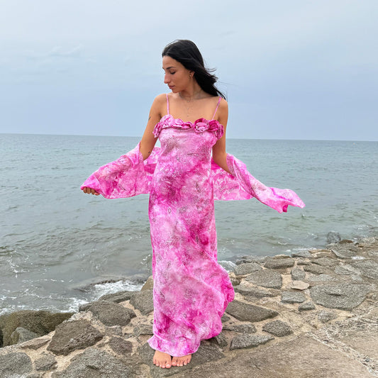 This vintage 2000s slip dress features a vivid pink tie-dye paisley print with rosette appliqué detail at the neckline. It flows into a long silhouette, ideal for summer weddings, proms, or formal parties, and comes with a matching scarf for versatile styling. A romantic archival piece made in France, perfect for bridal, evening, or statement occasions. Made from a non-stretch polyester blend. Excellent vintage condition.