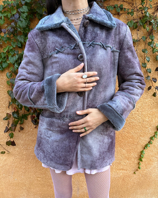 Vintage 2000s faux shearling coat in a rare purple-blue-gray tie-dye abstract finish. Features a soft faux fur collar and cuffs, button closure, side pockets, and decorative criss-cross stitch detailing for a dystopic, cyber-grunge aesthetic. The brushed faux-suede surface gives it a distressed Y2K look, while the straight silhouette makes it easy for winter layering and festival styling. A standout early-2000s piece for streetwear, weird-girl outfits, and bold cold-weather looks.