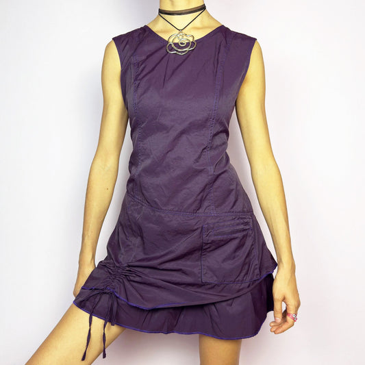 The Y2K Purple Layered Mini Dress is a vintage 2000s sleeveless dress in a deep purple hue, featuring a structured, layered silhouette, a side pocket, an adjustable drawstring ruched detail on the side for a customizable fit and a back zipper closure. Perfect for casual streetwear or edgy looks. Great vintage condition.