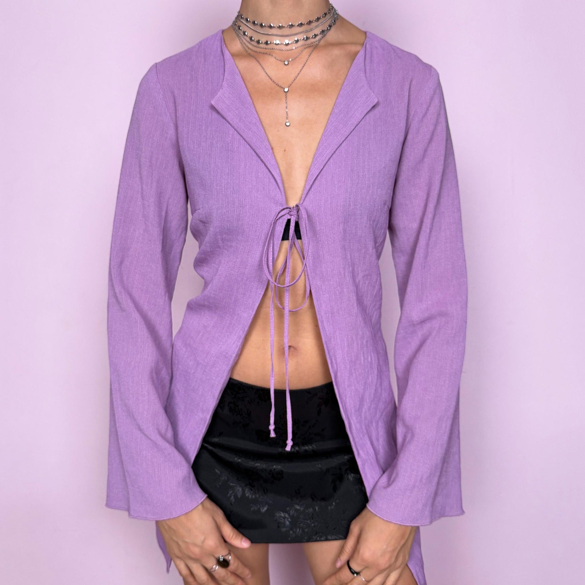 Vintage Y2K purple lilac tie front blouse from the 2000s with a flowy, lightweight feel. Features a deep V neckline with adjustable front ties, flared long sleeves, and a fluid silhouette ideal for layering. Dreamy fairy-inspired piece perfect for spring, summer, whimsical parties, or festival outfits. Made from a non-stretch fabric. Excellent vintage condition.