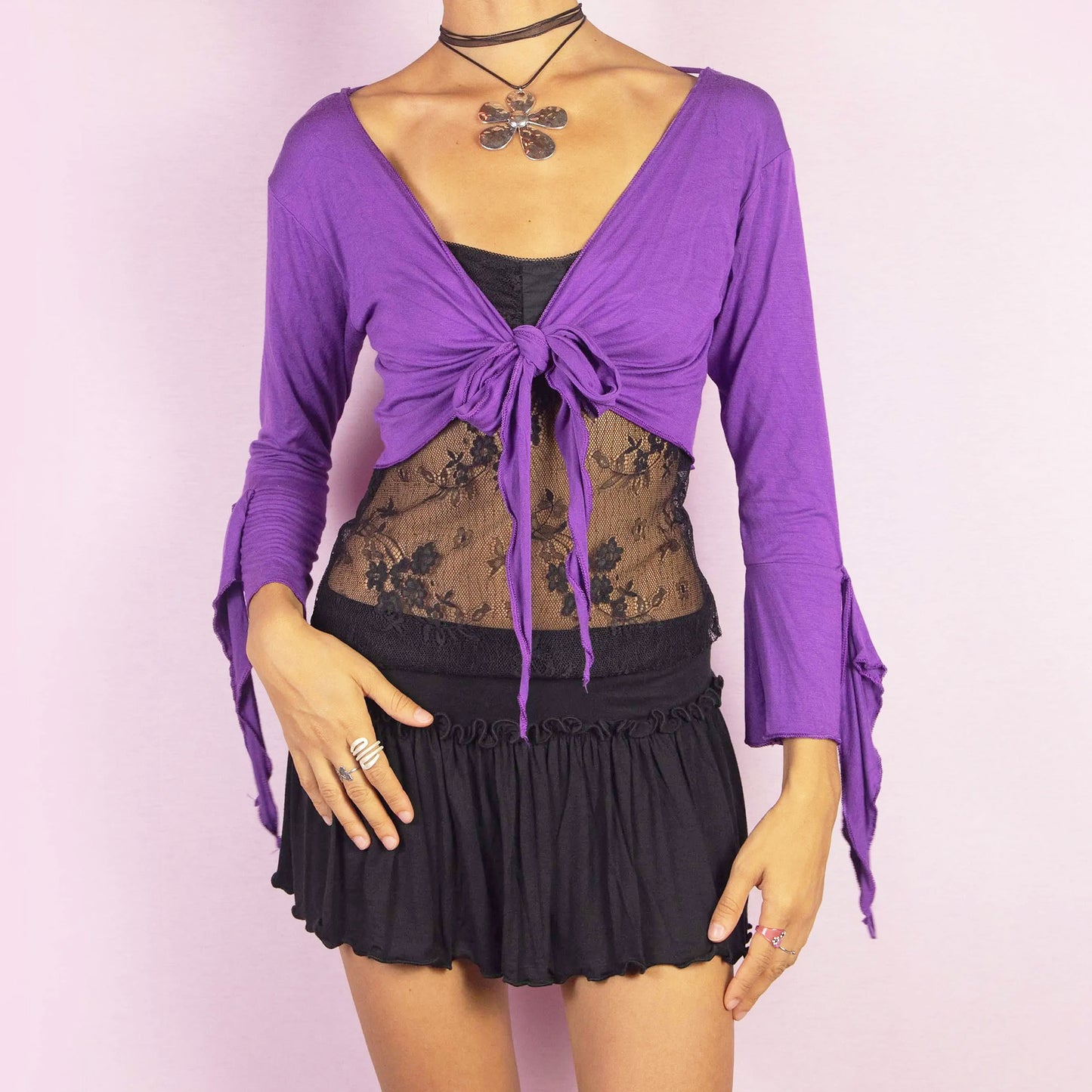 The Y2K Purple Tie Bolero is a vintage 2000s cropped cardigan featuring a vibrant purple color, front tie closure, and unique bell sleeves. The open-back design with criss-cross straps adds a playful touch, making it ideal for festival-inspired outfits.