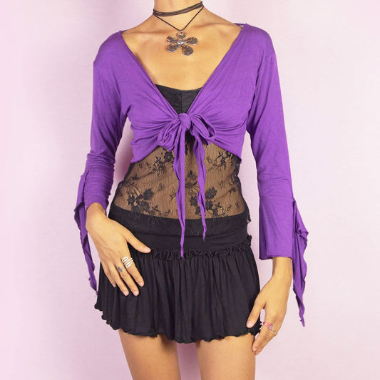 The Y2K Purple Tie Bolero is a vintage 2000s cropped cardigan featuring a vibrant purple color, front tie closure, and unique bell sleeves. The open-back design with criss-cross straps adds a playful touch, making it ideal for festival-inspired outfits.