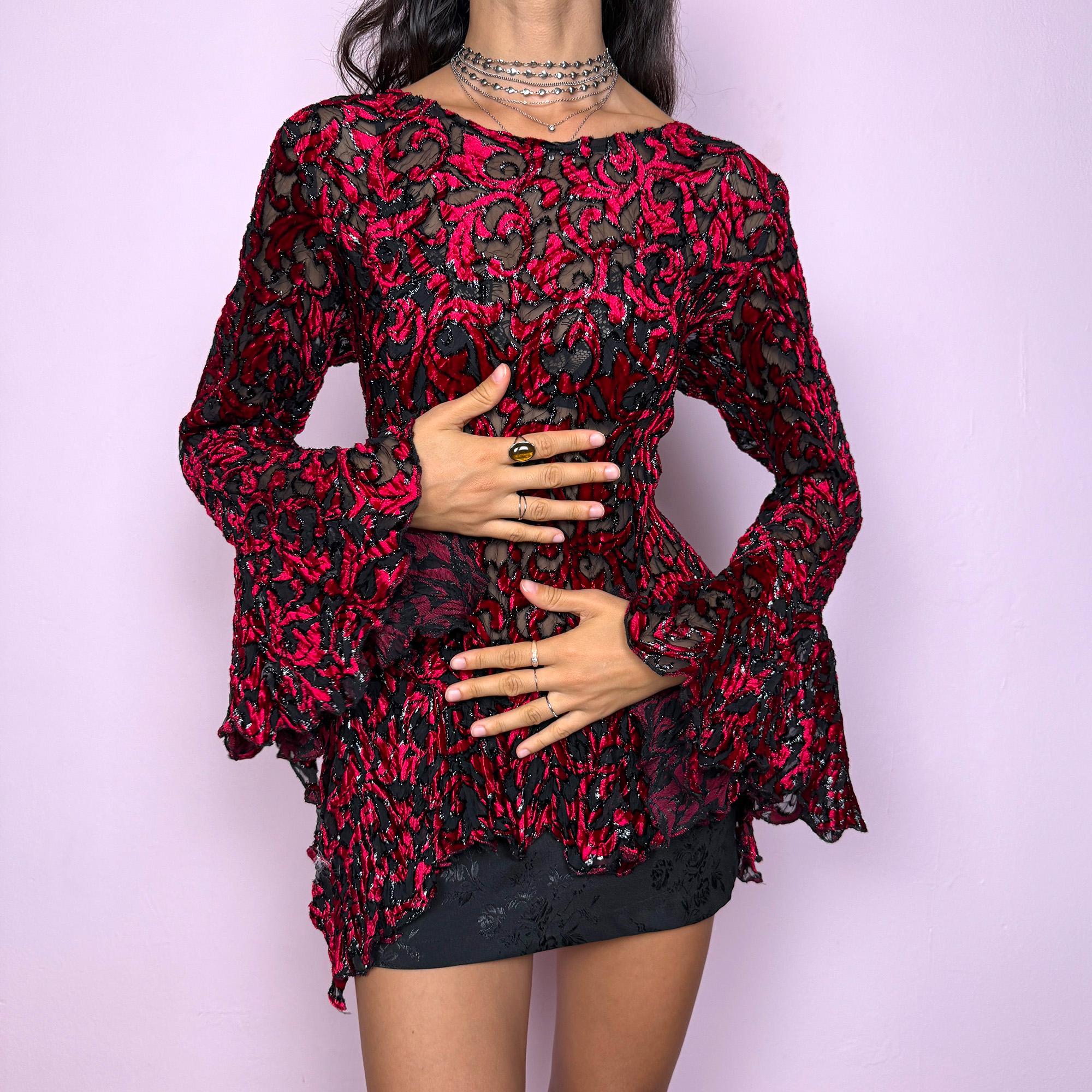 This vintage 2000s red and black devoré velvet top features a sheer burnout pattern with metallic threads, fitted bodice, asymmetric bell sleeves, and flared hem. The sculpted silhouette channels romantic gothic allure with Y2K glam energy. Perfect for evening styling, festivals, or statement layering—an archival French piece merging art and sensuality. Made from stretchy polyester devoré velvet blend. Excellent vintage condition.