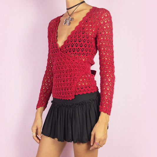 The Y2K Red Crochet Wrap Cardigan is a vintage 2000s piece featuring a romantic deep V-neckline with an intricate open-knit design. Its wrap style and tie closure at the back form a stylish bow, creating a flattering silhouette. Perfect for layering in spring and summer. Great vintage condition.