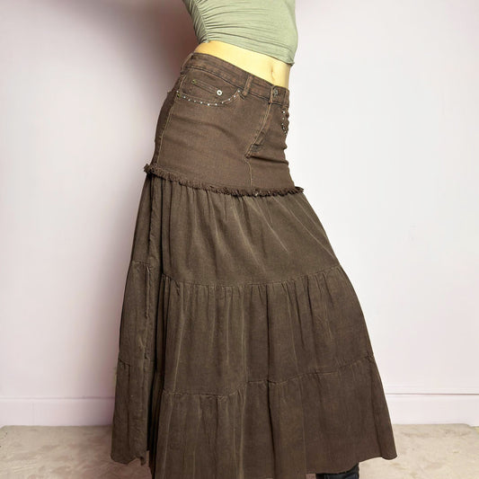 The Y2K Brown Tiered Midi Skirt is a vintage 2000s piece combining denim and soft corduroy for a unique mixed-fabric look. Featuring a stretchy waistband with rhinestone embellishments, pockets and a button-zipper closure, this skirt transitions into flowy tiered corduroy panels for a boho-inspired silhouette. Perfect for casual outfits.