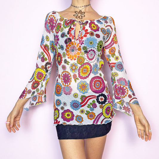 The Y2K White Floral Tie Front Top is a vintage 2000s piece bursting with color and retro charm. Features a vibrant multicolor 60s-inspired flower print on lightweight, slightly sheer pleated fabric. Designed with a flattering scoop neckline, keyhole front with tie closure, and flared bell sleeves. Stretchy and breathable – perfect for summer, festivals, or hippie styles. Great vintage condition.