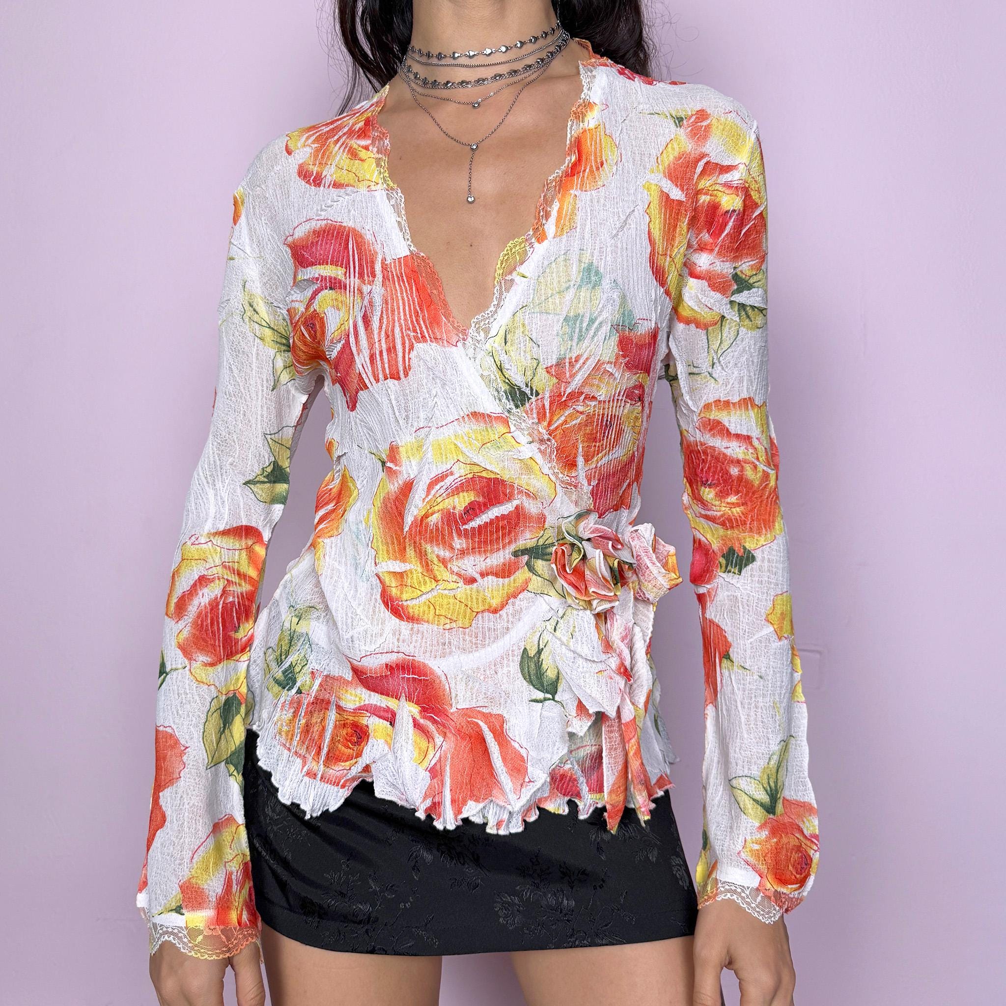 Dreamy vintage 2000s white wrap tie blouse with orange, red, and yellow rose floral print. Features lace trim, bell sleeves, crinkle pleated fabric, and rosette appliqué detail. Stunning deep V-neck top perfect for spring summer parties, formal or outdoor events. Made from stretchy polyester by a French brand. Excellent vintage condition.